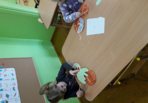 Dzieci przy stolikach naklejają elementy dekoracyjne na pączki.