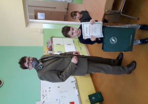 Chłopiec obok pana leśniczego prezentuje zwycięski dyplom i nagrody.