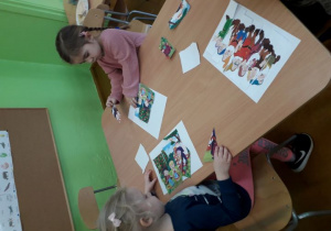 Dziewczynki przy stoliku składają i naklejają elementy baśniowych puzzli.