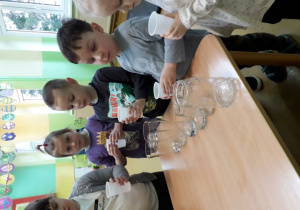 Przedszkolaki przy stoliku przeprowadzają doświadczenie związane z pomiarem objętości cieczy.