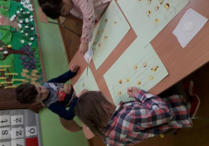 Dzieci przy stoliku naklejają wesołe nutki na pięciolinię.