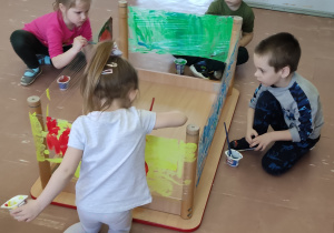 Grupa dzieci maluje farbami na folii spożywczej.