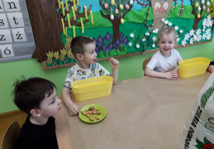 Dzieci przy stoliku sadzą cebulkę.