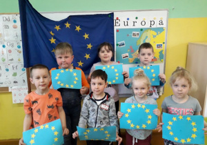 Dzieci na tle flagi Unii Europejskie prezentują wykonane przez siebie flagi.
