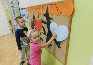 Dzieci z grupy 3,4 latków stojące przy tablicy i losujące imiona z serduszek