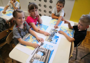 Dzieci siedzące przy stolikach i oglądające ilustracje