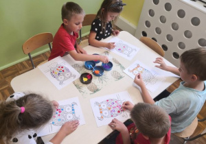 Dzieci siedzące przy stoliku i malujące farbami kropeczkowe sowy