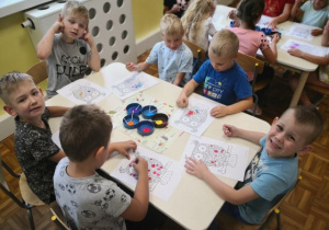 Chłopcy siedzący przy stoliku i malujący farbami kropeczkowe sowy