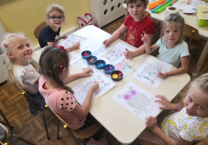 Dziewczynki siedzące przy stoliku i malujące farbami kropeczkowe sowy