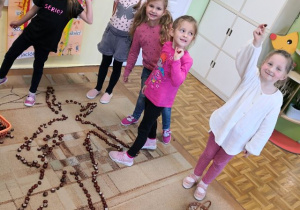Dziewczynki prezentujące sylwetę koleżanki ułożoną z kasztanów na dywanie