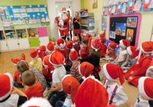 Dzieci ubrane na czerwono w czerwonych czapeczkach witające Mikołaja