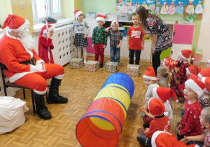 Dzieci biorące udział w konkursie przechodzenia przez tunel z prezentami i siedzący na krześle Mikołaj