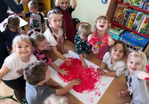 Przedszkolaki odbijające dłonie umoczone w czerwonej farbie na sylwecie dużego jabłka