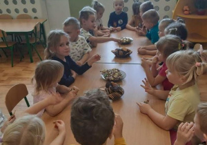 Grupa 3,4,5-latków siedząca przy stolikach i częstująca się słodkościami