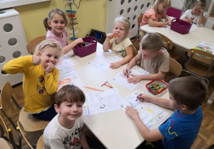 Dzieci z grupy 3,4,5-latków siedzące przy stoliku i kolorujące obrazek tematyczny