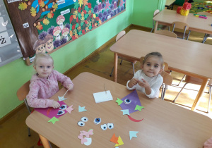 Dzieciaki przy stolikach konstruują latawce z kolorowych elementów.