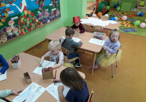 Dzieci przy stolikach kolorują ilustracje.