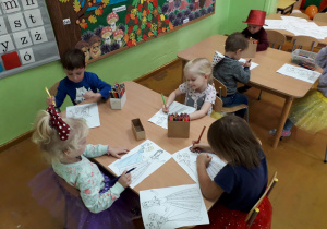 Dzieci przy stolikach kolorują ilustracje.