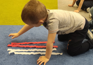 Dzieci układają Flagę Polski z pasków bibuły.