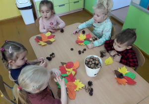 Dzieci wykonują jesienne stroiki z liści , kasztanów i orzechów.
