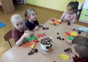 Dzieci wykonują jesienne stroiki z liści , kasztanów i orzechów.