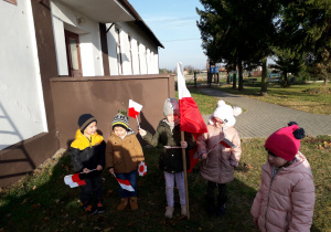 Dzieci uczestniczą w zawieszeniu flagi na budynku przedszkola.