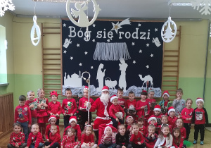 Przedszkolaki z Mikołajem na tle dekoracji przedszkolnej.