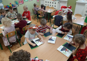 Przedszkolaki siedzące przy stolikach i rysujące na tabletach.