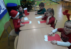 Dzieci przy stolikach ozdabiają skarpetę na prezenty.