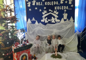Dzieci w odświętnych strojach na tle dekoracji świątecznej.