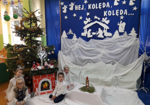 Dzieci w odświętnych strojach na tle dekoracji świątecznej.
