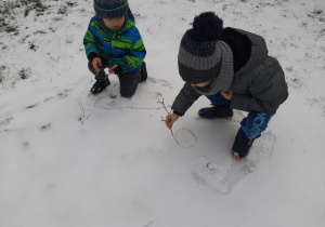Dzieci rysujące patykami na śniegu