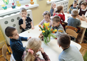 Dzieci siedzące przy kolejnym stoliku podczas słodkiego poczęstunku. Na stole stoi bukiet tulipanów.