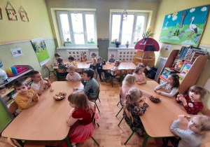 Dzieci z grupy 5,4,3 latków siedzące przy stolikach podczas słodkiego poczęstunku.