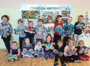 Dzieci z grupy 3,4,5 latków, na tle gazetki o dniu motyla, prezentują pomalowane kolorowymi farbami szablony motyli