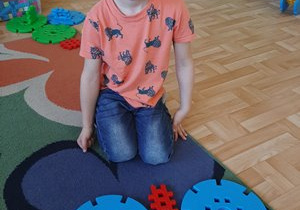 Chłopiec prezentujący motyla ułożonego z dużych plastikowych klocków konstrukcyjnych.