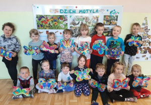 Dzieci na tle gazetki o dniu motyla prezentują pomalowane farbami szablony motyli.