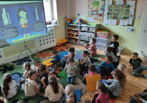 Grupa dzieci siedząca przed rozkładanym ekranem oglądająca prezentację multimedialną o kosmosie