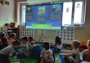 Grupa dzieci siedząca przed rozkładanym ekranem oglądająca prezentację multimedialną o kosmosie, inne ujęcie