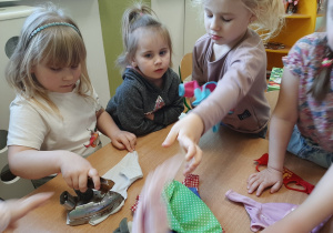 Grupa dziewczynek bawiąca się w prasowanie starym żelazkiem ubrań dla lalek, inne ujęcie.