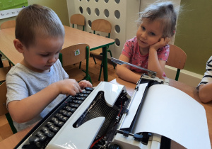Chłopiec piszący na maszynie, dziewczynka przyglądająca się czynności.