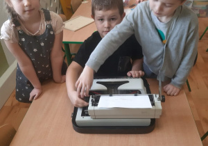 Grupa dzieci bawiących się maszyną do pisania.