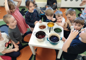 Grupa dzieci 3,4,5 letnich wokół stolika, na którym stoją naczynia z naturalnymi barwnikami do jajek.