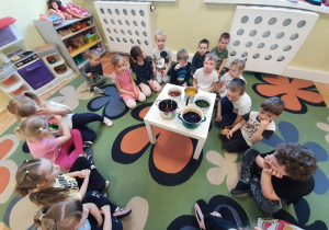 Grupa dzieci 3,4,5 letnich wokół stolika, na którym stoją naczynia z naturalnymi barwnikami do jajek, kolejne ujęcie.