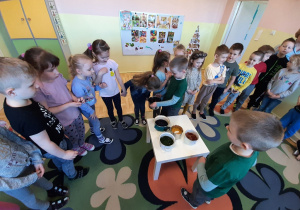 Chłopiec pokazuje innym dzieciom z grupy ustawionym w rzędzie naczynie z naturalnym barwnikiem do jajek.