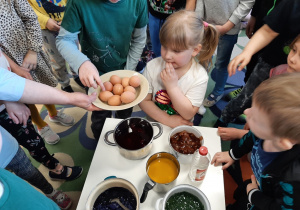 Dzieci wokół stolika z barwnikami do jajek. Będą umieszczać w naczyniach jajka i przygotowywać kraszanki.