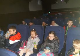 Przedszkolaki z grupy 5-6 latków siedzą na fotelach w kinie i czekają na rozpoczęcie seansu
