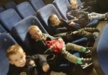 Chłopcy z młodszej grupy siedzą na fotelach w kinie i czekają na rozpoczęcie filmu
