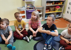 Kilkoro dzieci z grupy 3,4,5 latków siedzi na dywanie i wykonuje ćwiczenia języka.