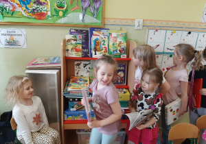 Grupa dzieci ustawiona przy przedszkolnym kąciku czytelniczym, bawi się w bibliotekę.